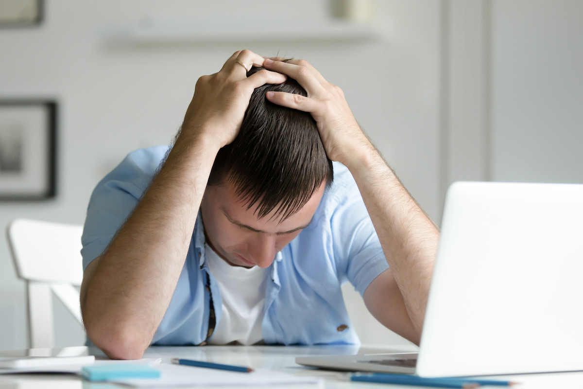 I can't do this! Man holding his head in despair by a laptop computer