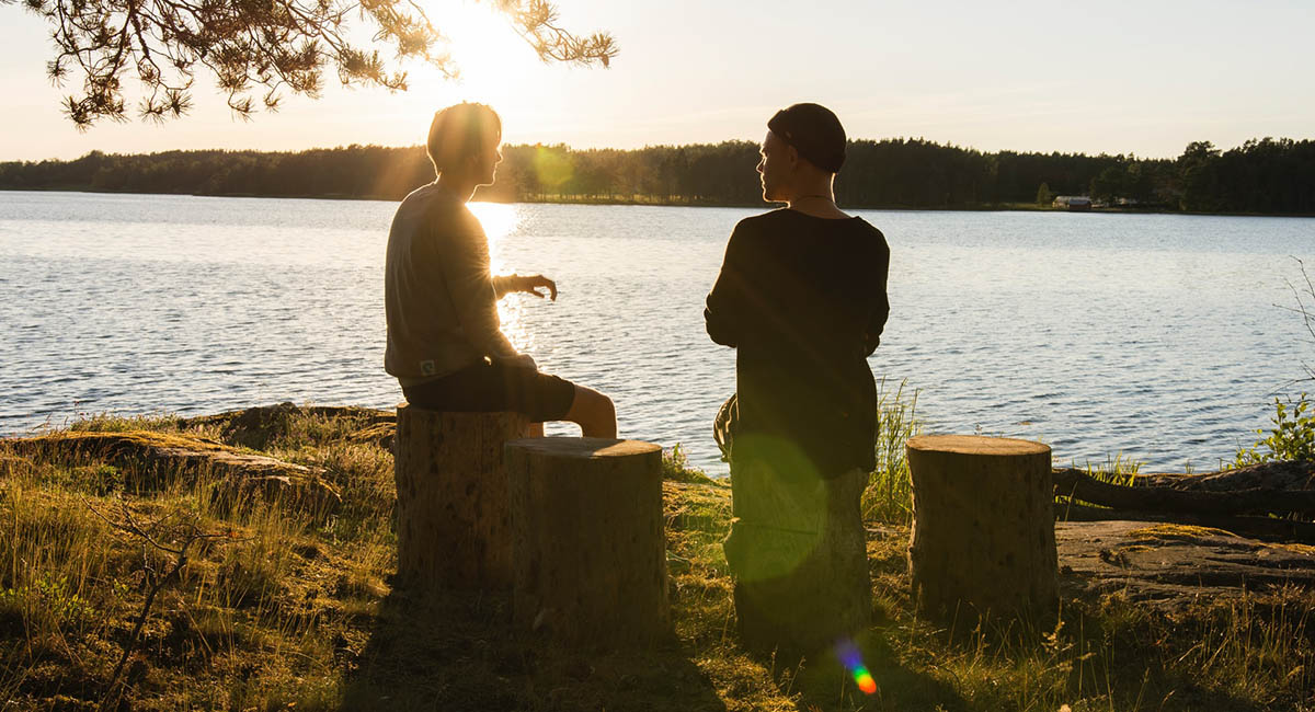 Two young men sitting by a lake talking