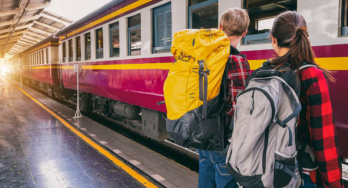 woman and man waiting on train track with backpacks