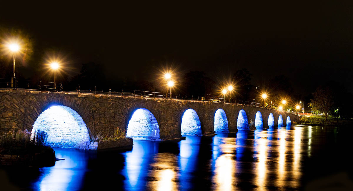 Stone bridge over water at night with lights, blue, yellow