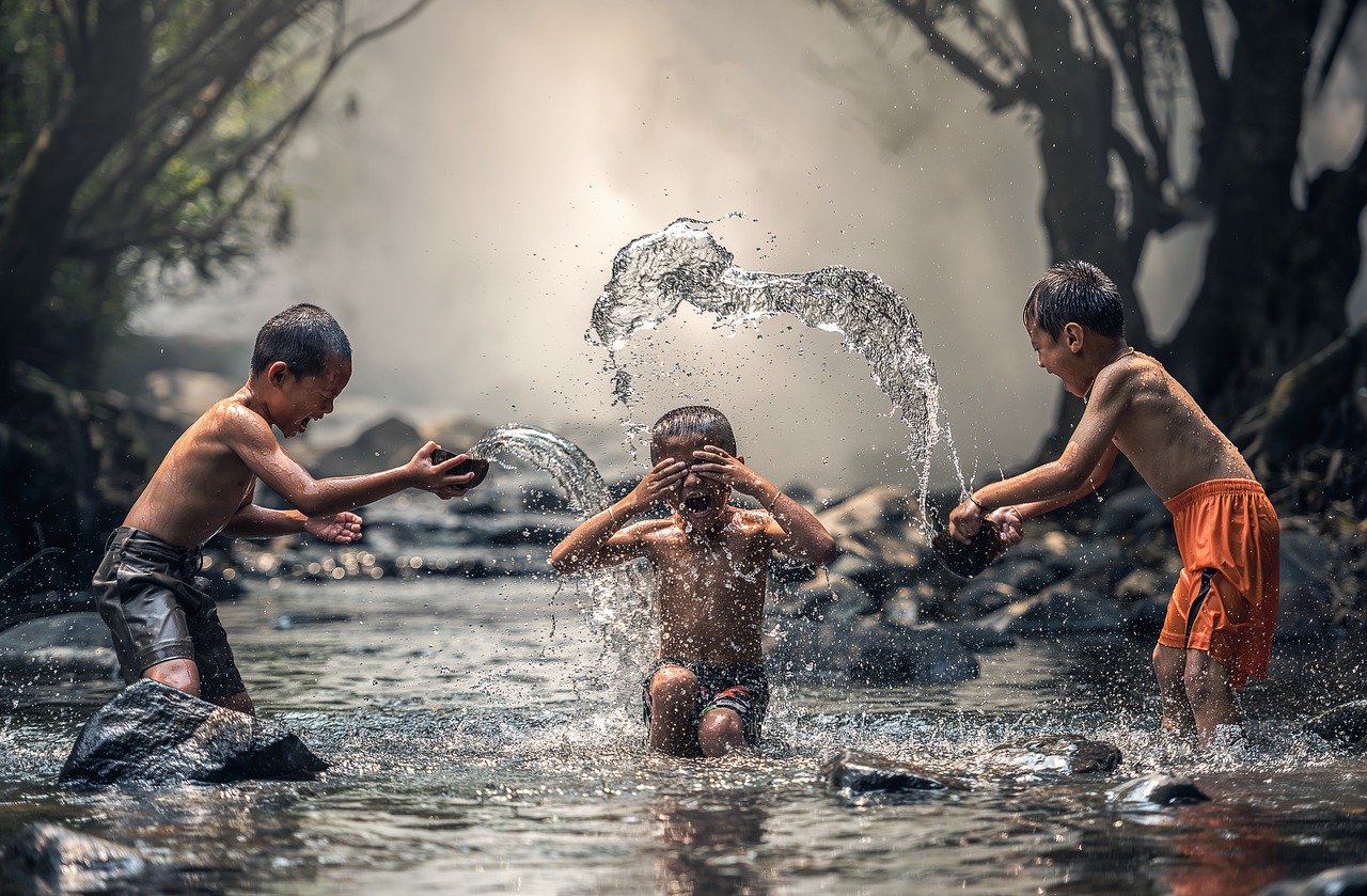 Ow! You got it in my eyes! Three boys playing in a river, splashing each other