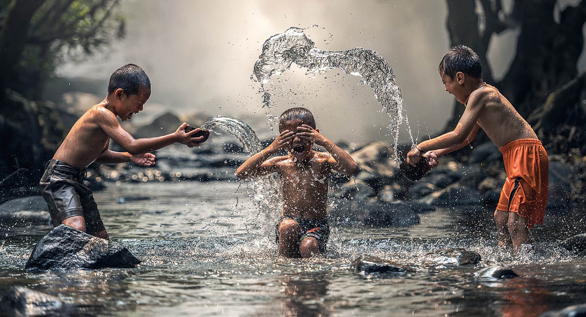 three young boys splashing each other in a stream