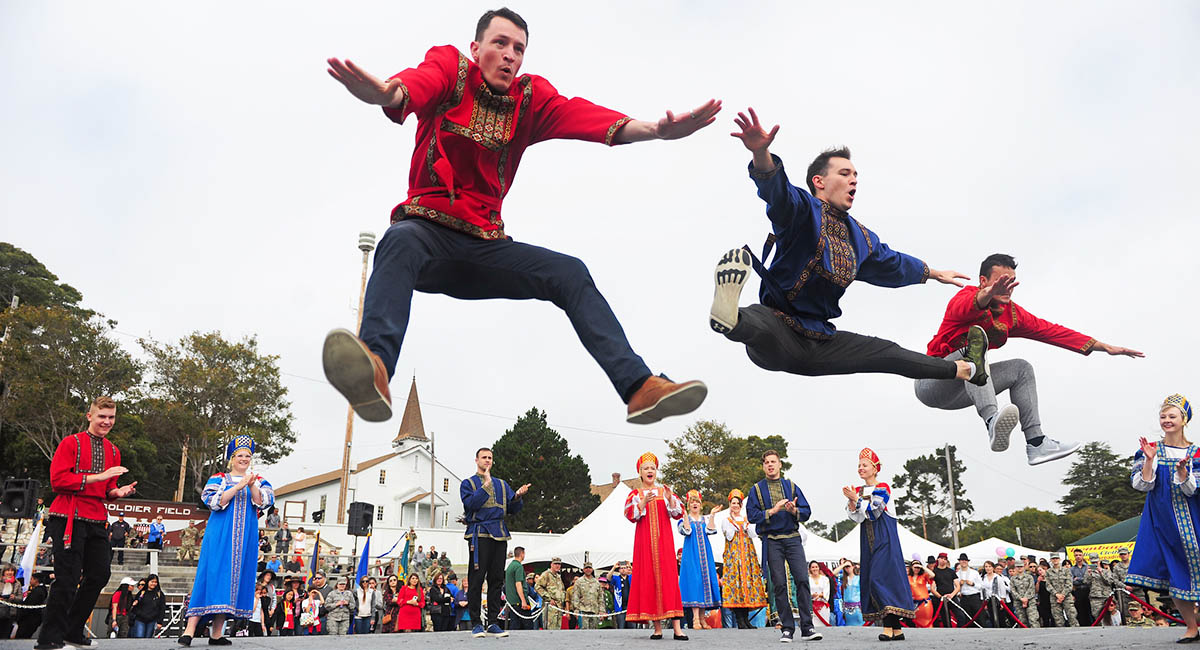 Men in ethnic costumes leaping in the air during a traditional dance.