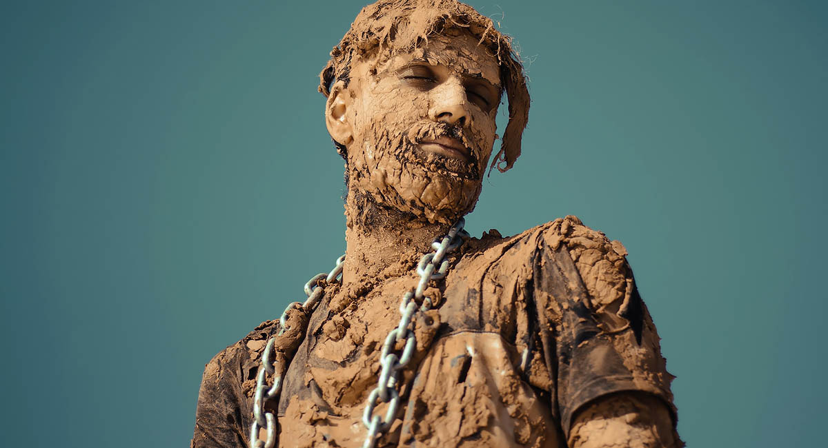 man covered in dried mud with industrial chain around his neck