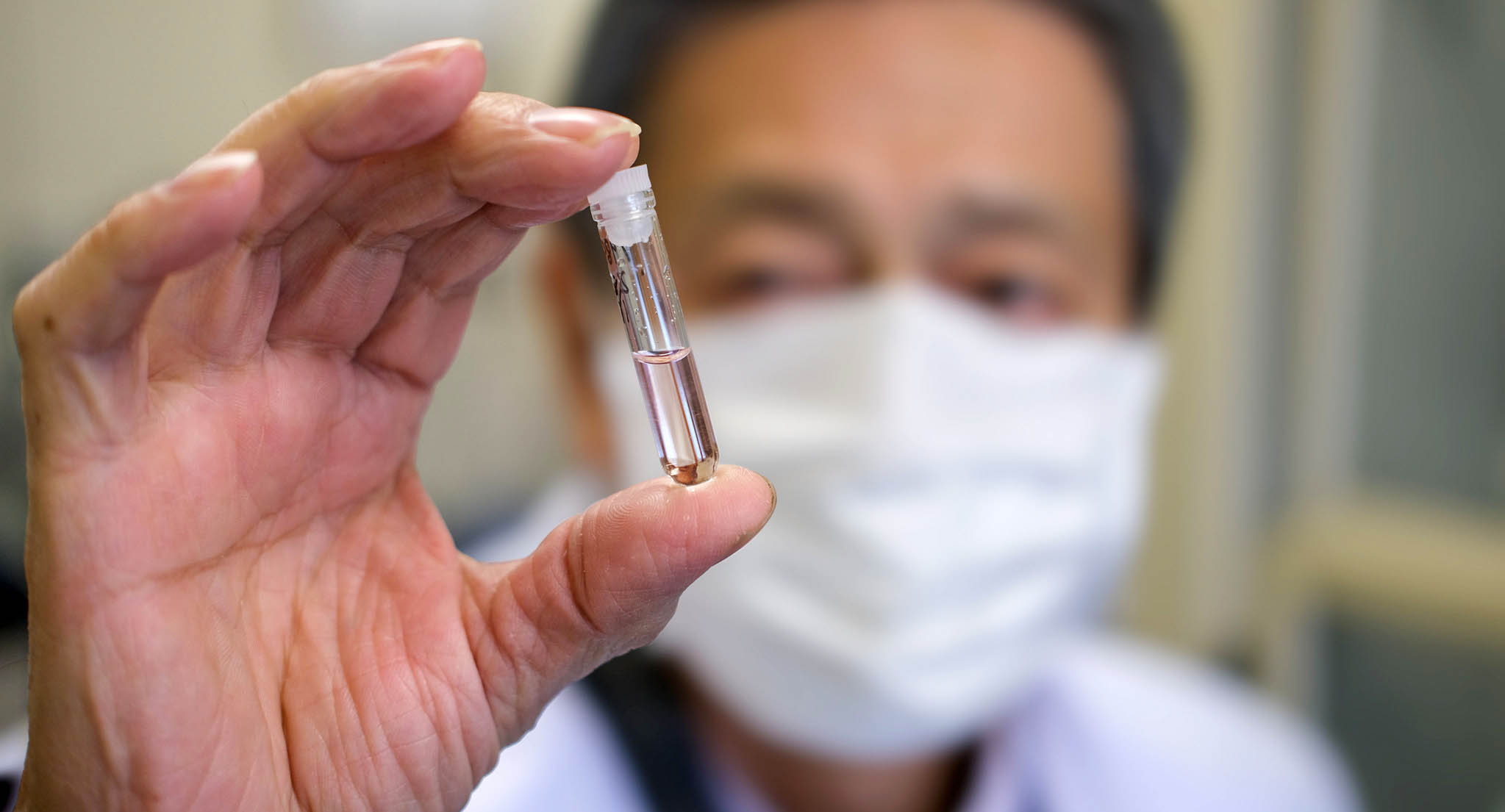 Japanese doctor holding small vial in front of blurred face