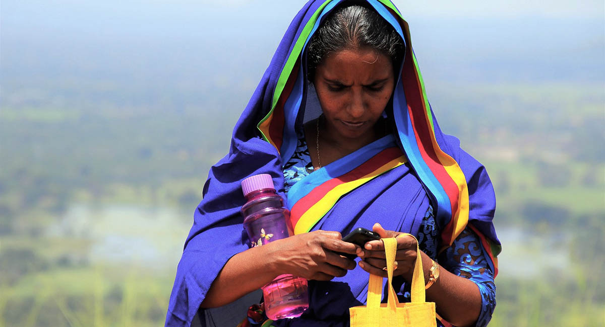 woman in colorful sari looking at cellphone, blurred landscape in background