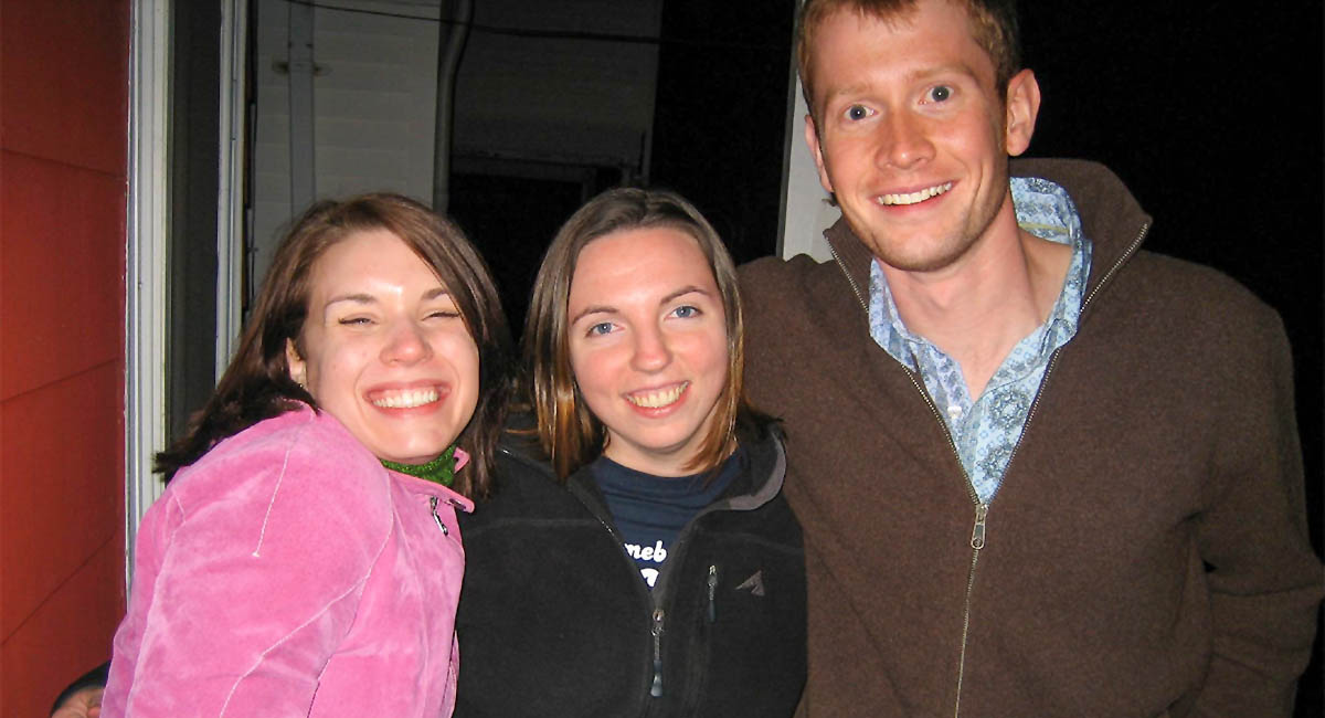 two young women with one young man standing with arms around each other smiling