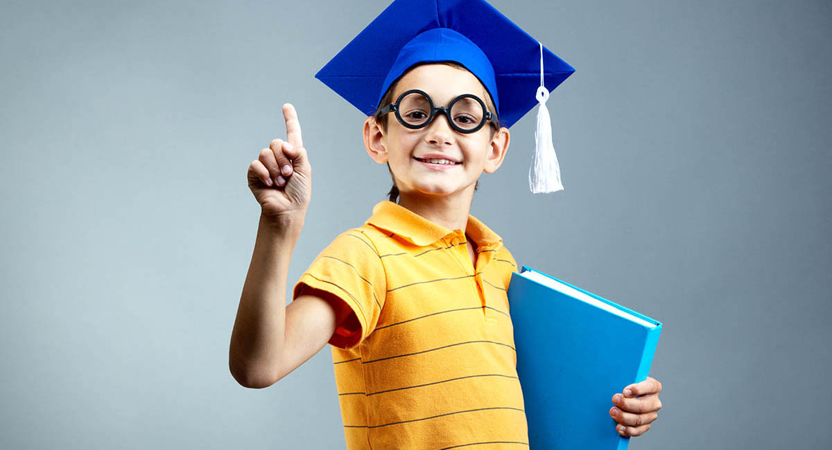 Young White boy wearing graduation cap, holding notebook, index finger pointing up