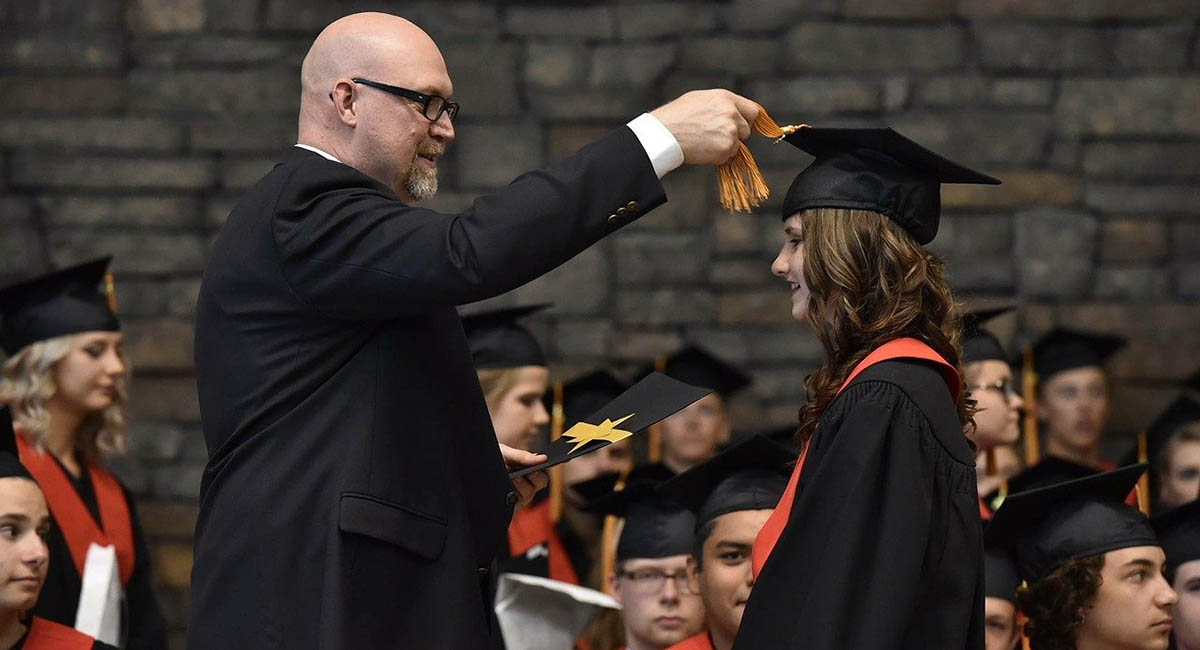 White man pulling tassel on young White woman's graduation mortarboard to the other side, graduation