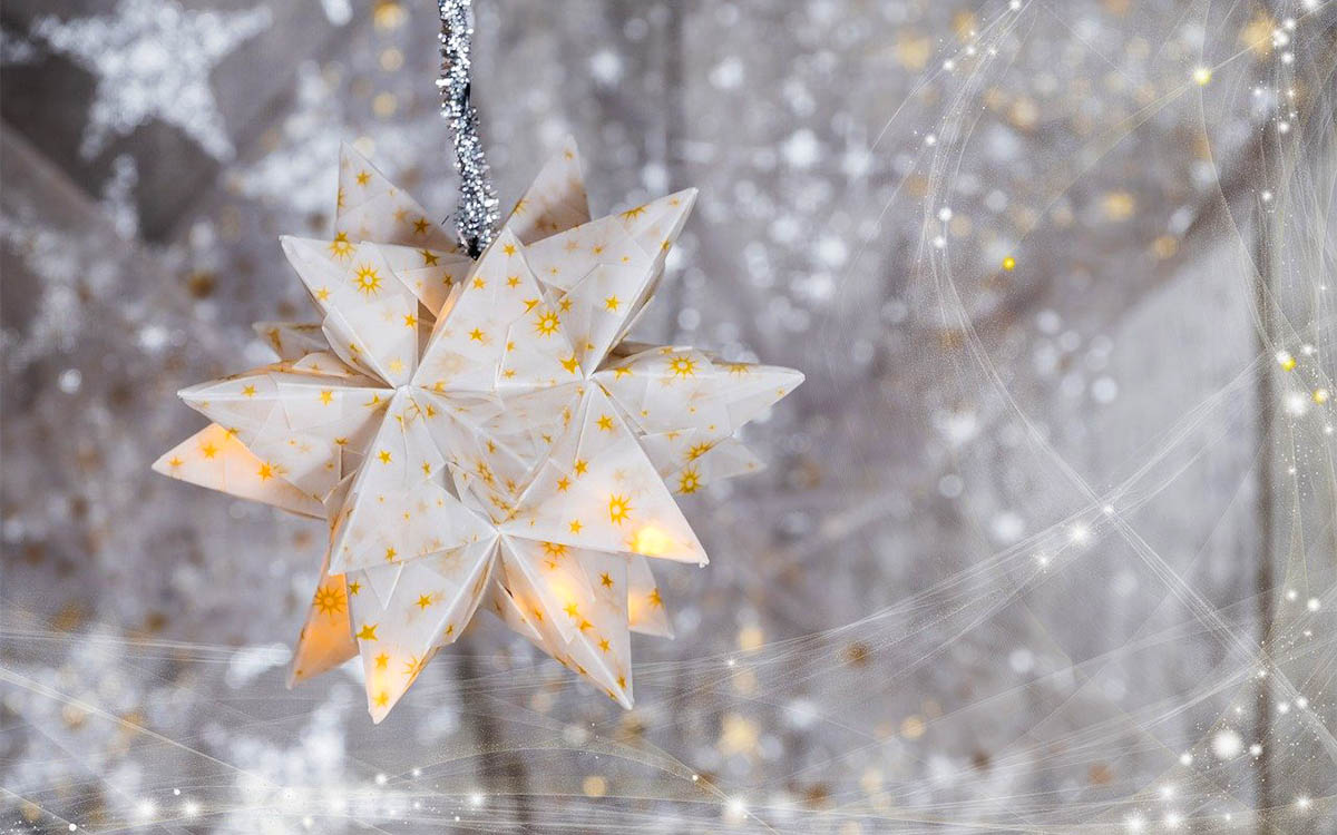 Winter holidays Paper star hanging in front of blurred strings of lights