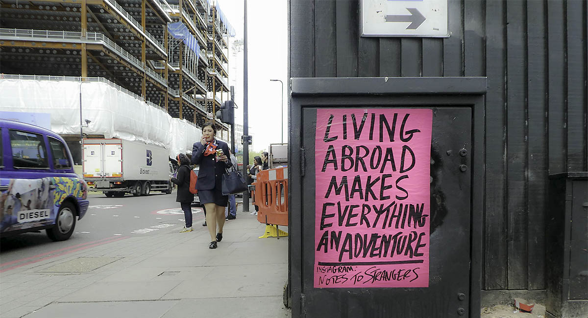 Sign on metal box along the street that says "Living abroad makes everything an adventure"