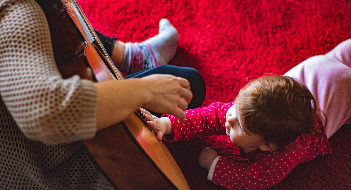 baby on floor reaching to touch guitar in adult's lap