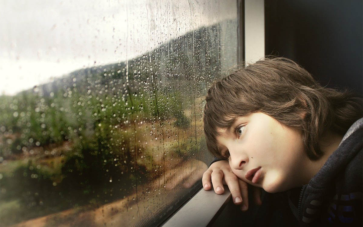 I'd rather be home. child looking out train window in the rain with a sad expression