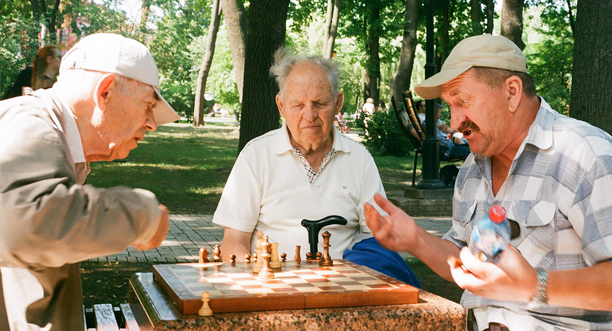 Three older White men playing chess in a park