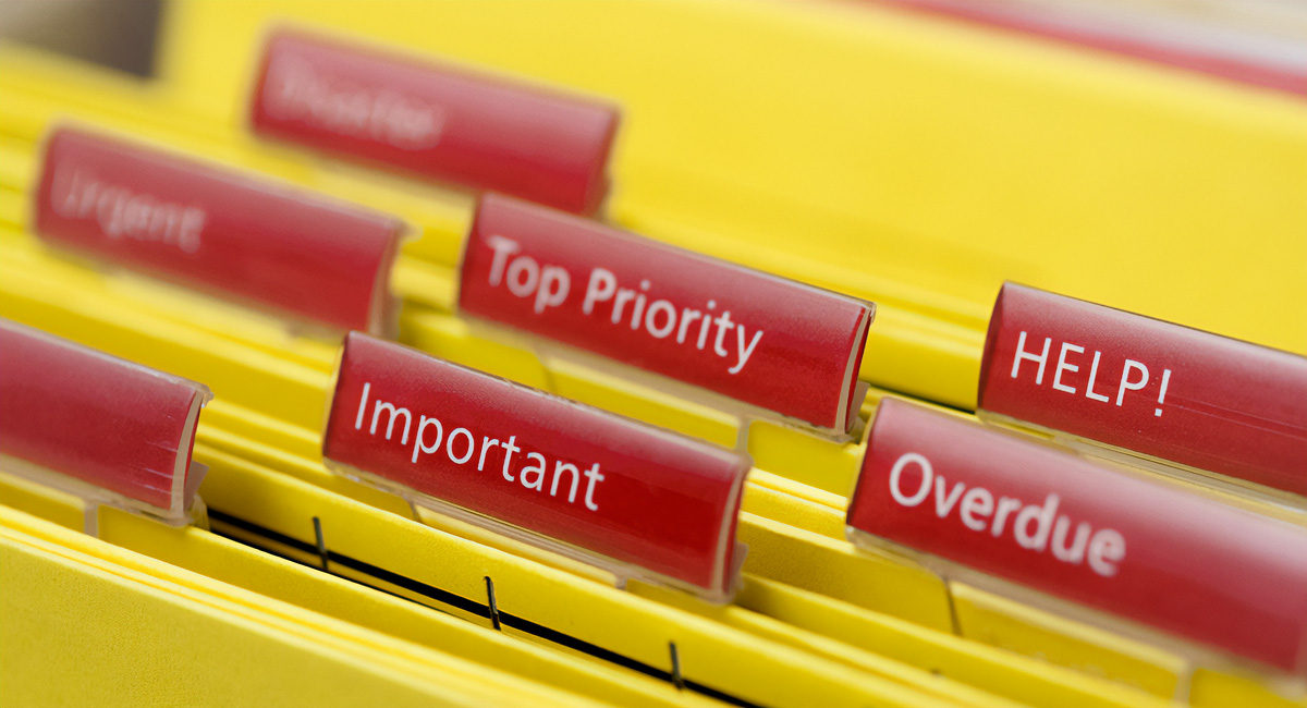 yellow hanging file folders with red labels "important" "top priority" "overdue" "HELP!"