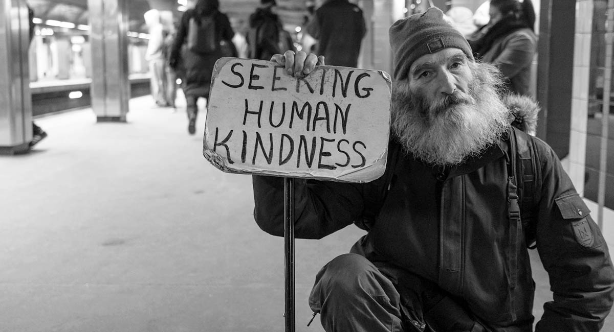 Homeless man holding sign "Seeking human kindness"