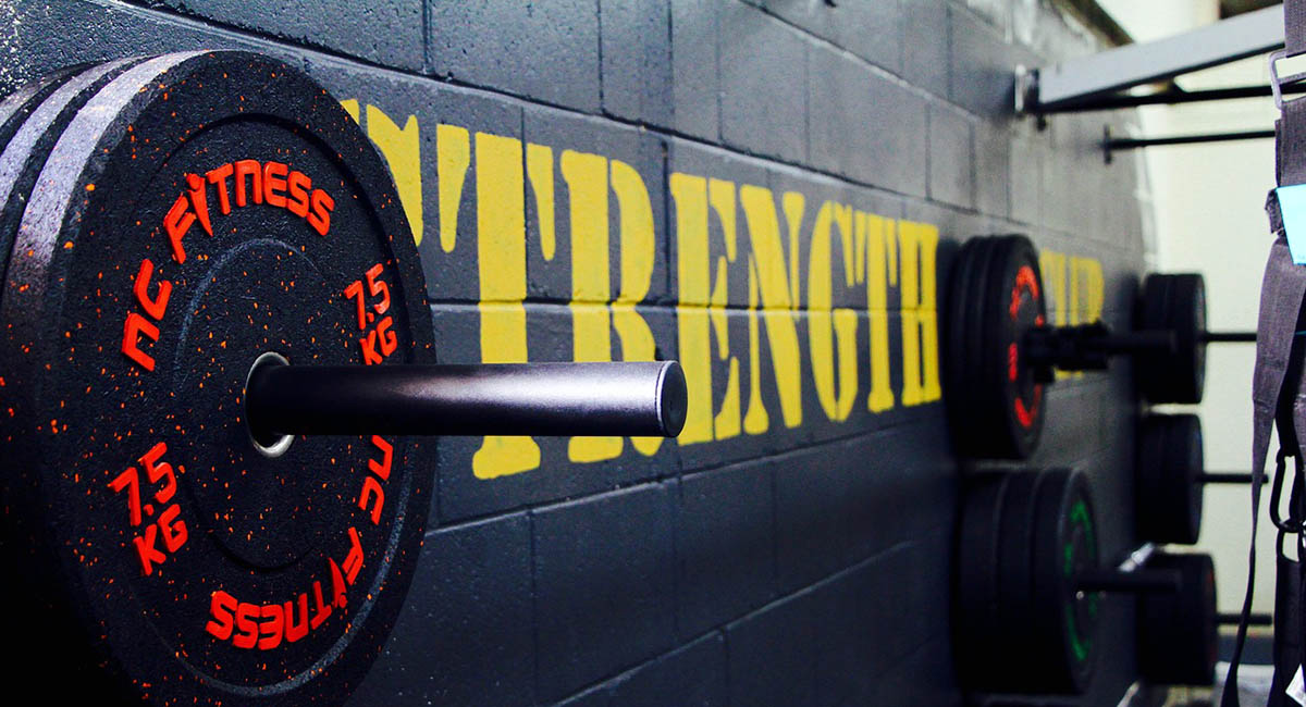 barbell weights against wall that says STRENGTH