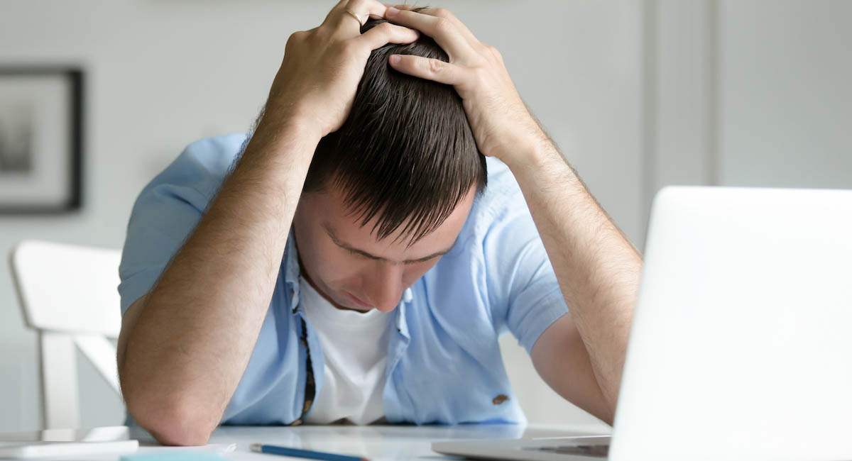 Man holding his head in despair by a laptop computer