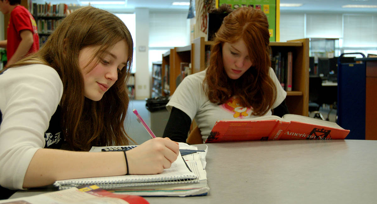 Two White teenage girls studying at a table in a library