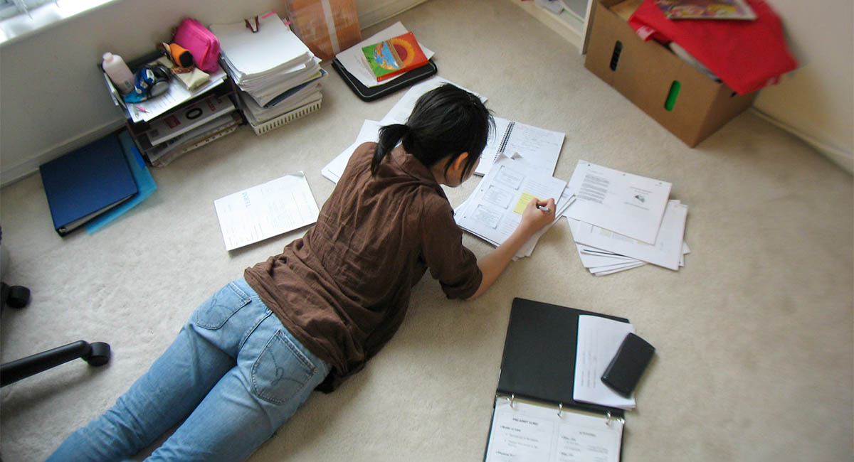 young woman lying on dorm room floor studying