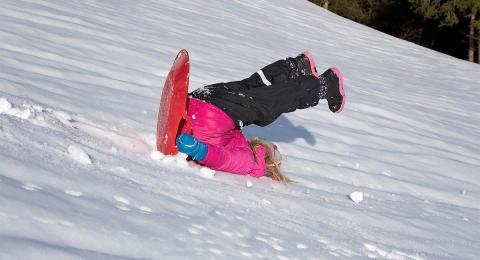 Child falling off a toboggan and sliding downhill backwards on her head