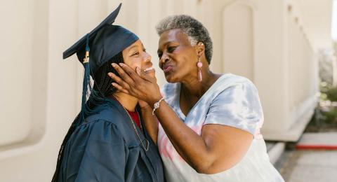 Woman graduate in cap and gown being kissed by her mother