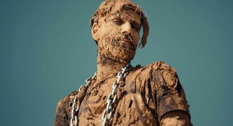 man covered in dried mud with industrial chain around his neck