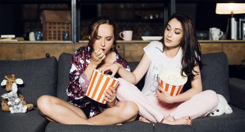 Two young women eating popcorn with one of them grabbing popcorn out of the other's bucket