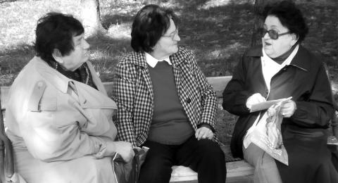 Three older women seated on a park bench, talking