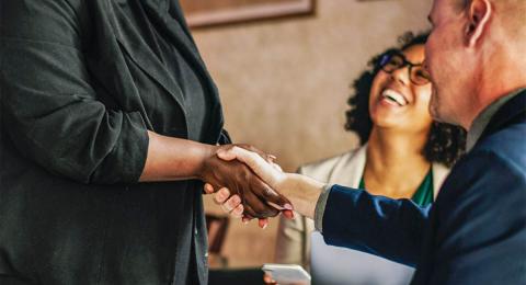 Woman and man shaking hands with woman laughing in the background, diversity