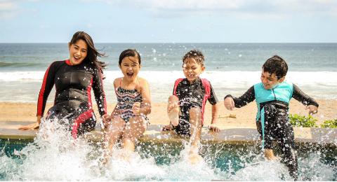 Group of children sitting on the edge of a pool by a beach splashing with their feet