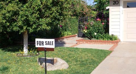 FOR SALE sign in front of corner of house with garden