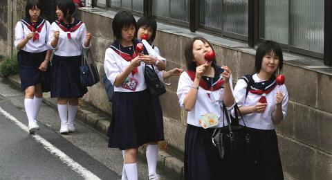 Junior high students in Japan, girls, walking on a street in school uniforms, eating candy apples