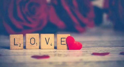 Scrabble tiles spelling LOVE, small red heart, blurred background roses