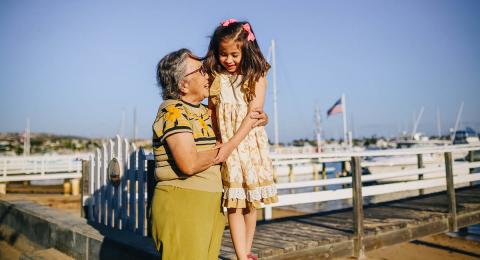 Older woman holding young girl who's standing on a low wall