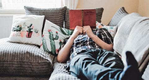 Person lying on a couch with a book in front of their face