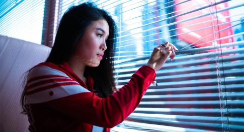 Young woman looking out a window through venetian blinds
