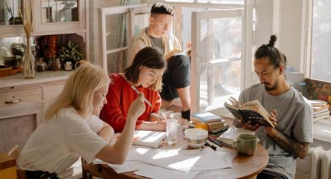 Four young people sitting at a table in an apartment doing different things