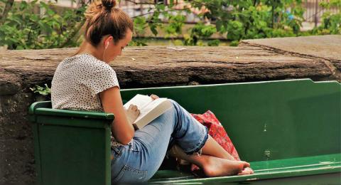 Young woman on a bench reading with earphones on