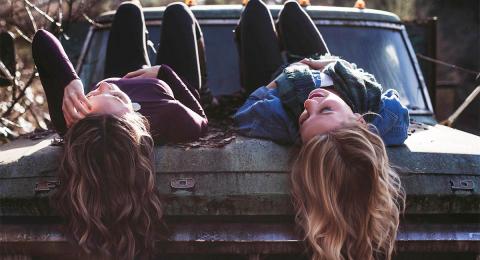 two young women lying on their backs on the hood of an old car with their hair hanging down