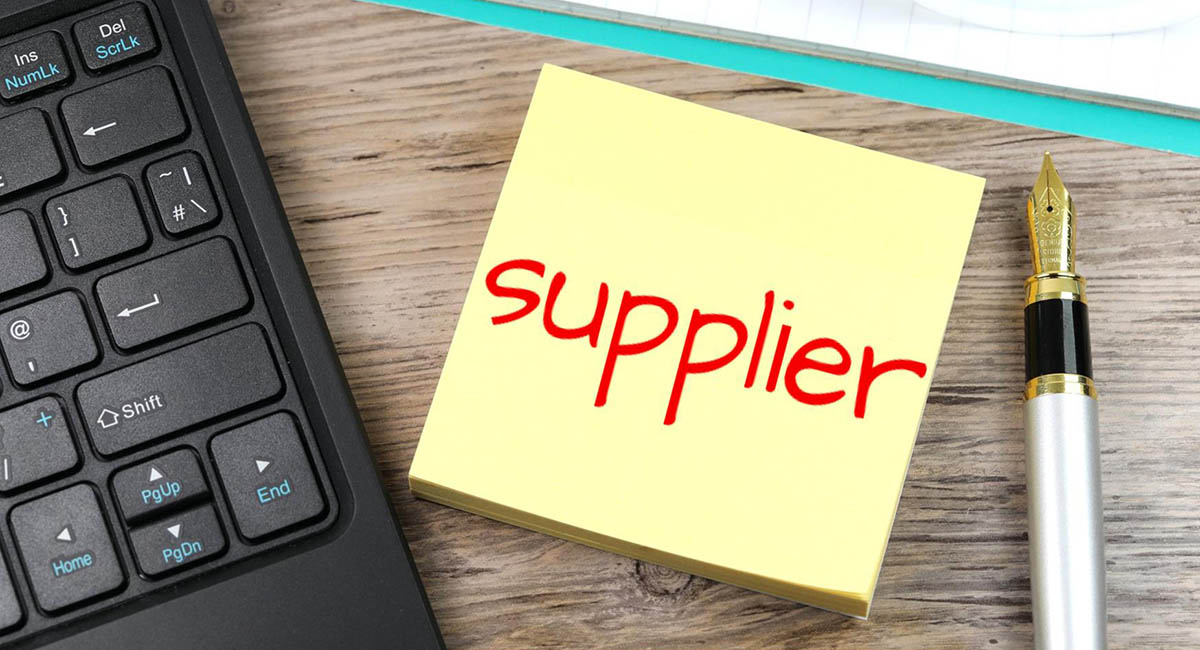 post-it note with word "supplier" on desk next to computer keyboard and fountain pen