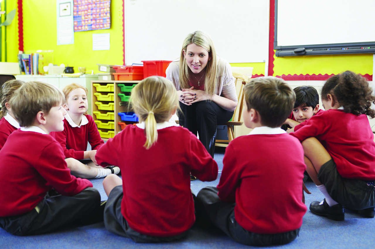 Tell me more! Teacher with circle of young students sitting on the floor around her