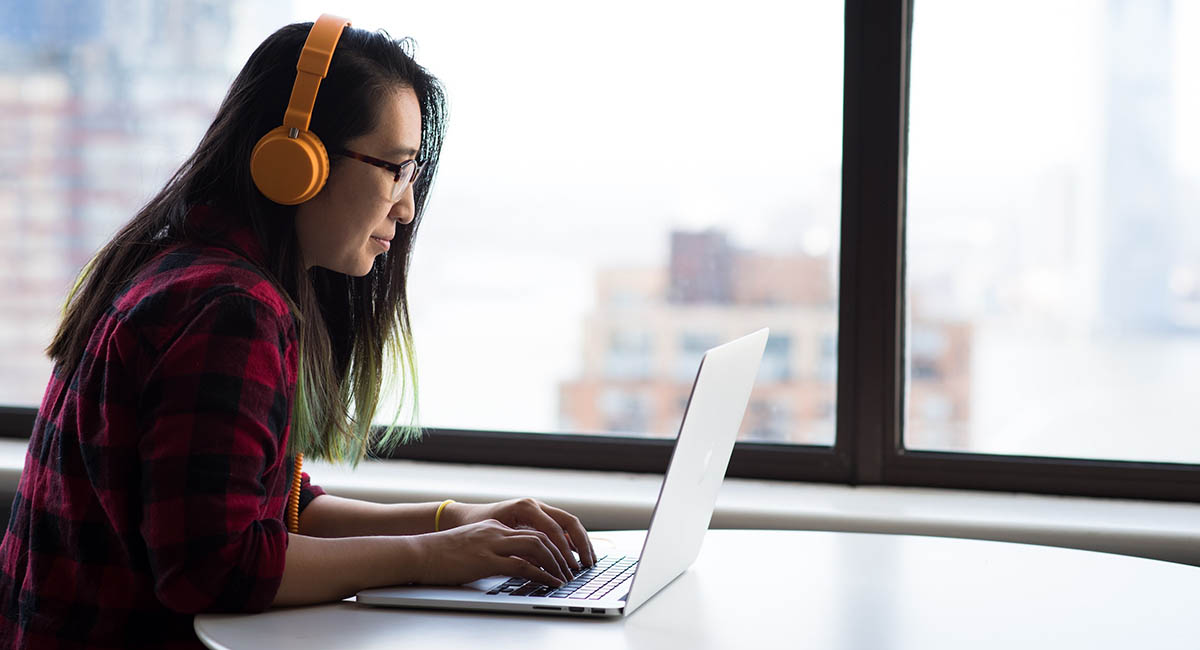 woman working on laptop with headphones on by window
