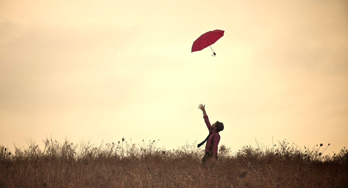 A man throwing a red umbrella in the air