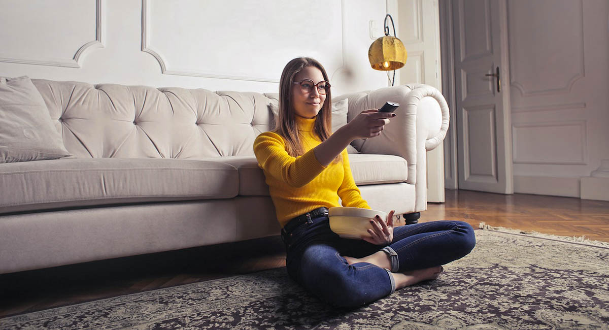 Young woman with remote and bowl in lap